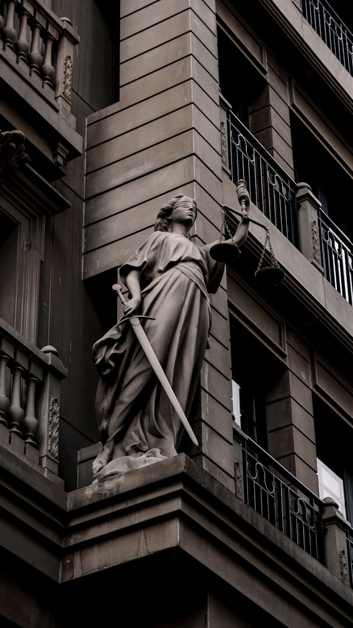 A sculpture of Lady Justice with a sword and scales on a city building's facade.
